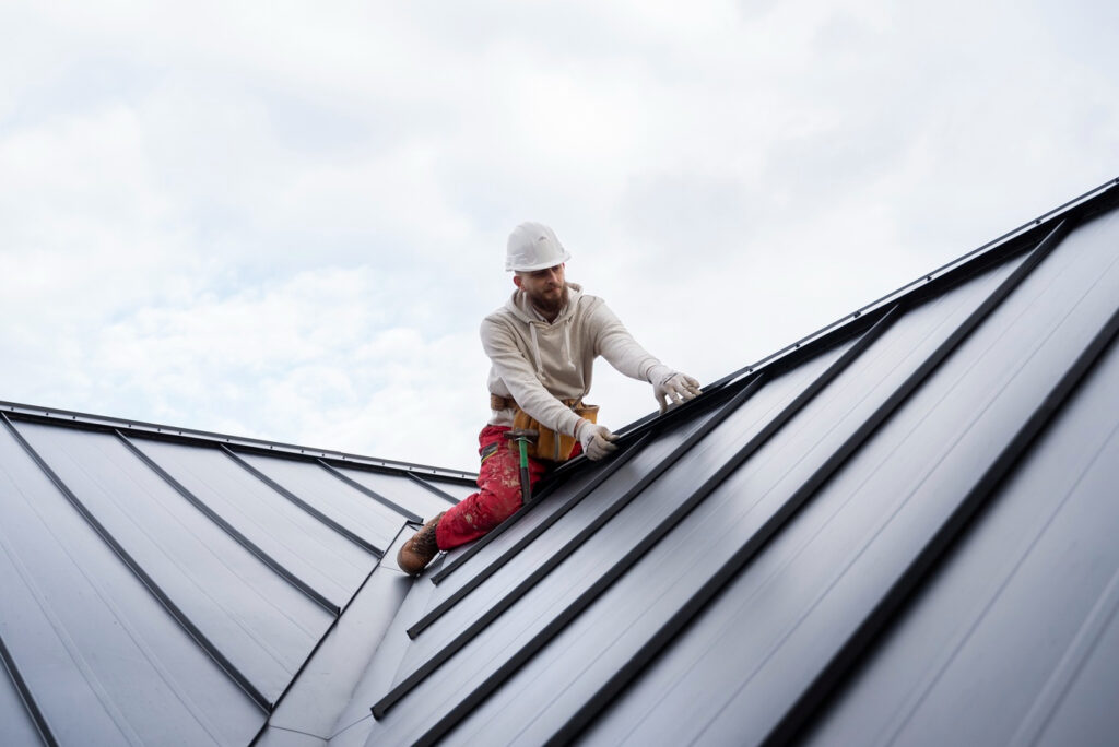 Worker installing metal roof panels on a building.