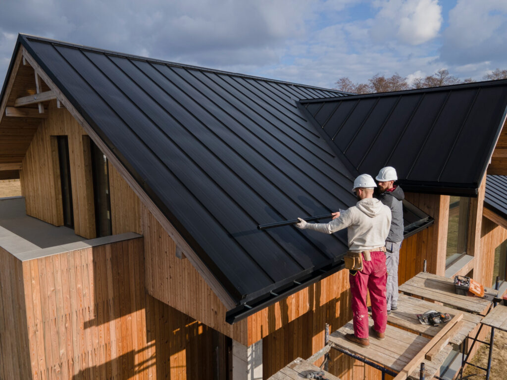 Workers installing black metal roof on modern wooden house