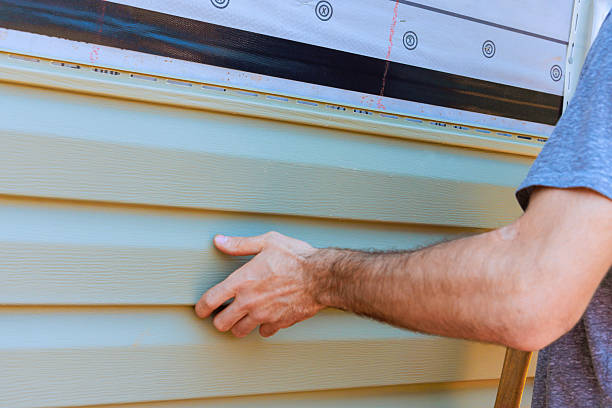 Person installing vinyl siding on a house wall.
